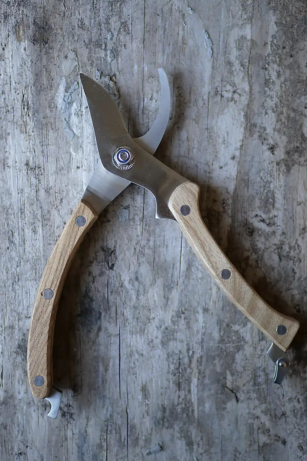 A pair of pruning shears with light-coloured wooden handles and a stainless steel blade, resting on a weathered grey wooden surface.