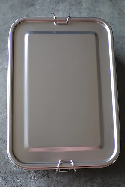 A rectangular stainless steel lidded container  with two metal clasp handles, shown from a top-down perspective on a gray concrete floor.