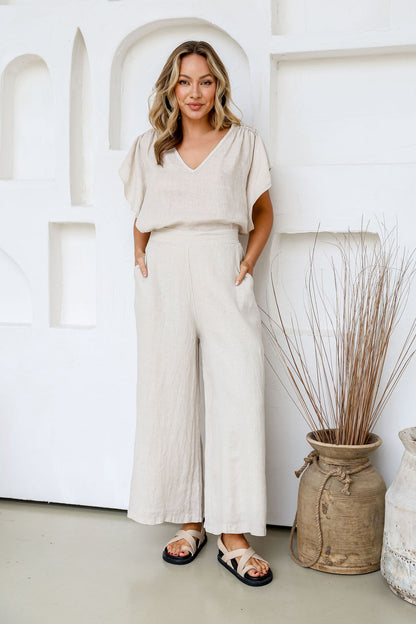 Woman in a sand-coloured outfit standing in a minimalistic room with decorative plants.