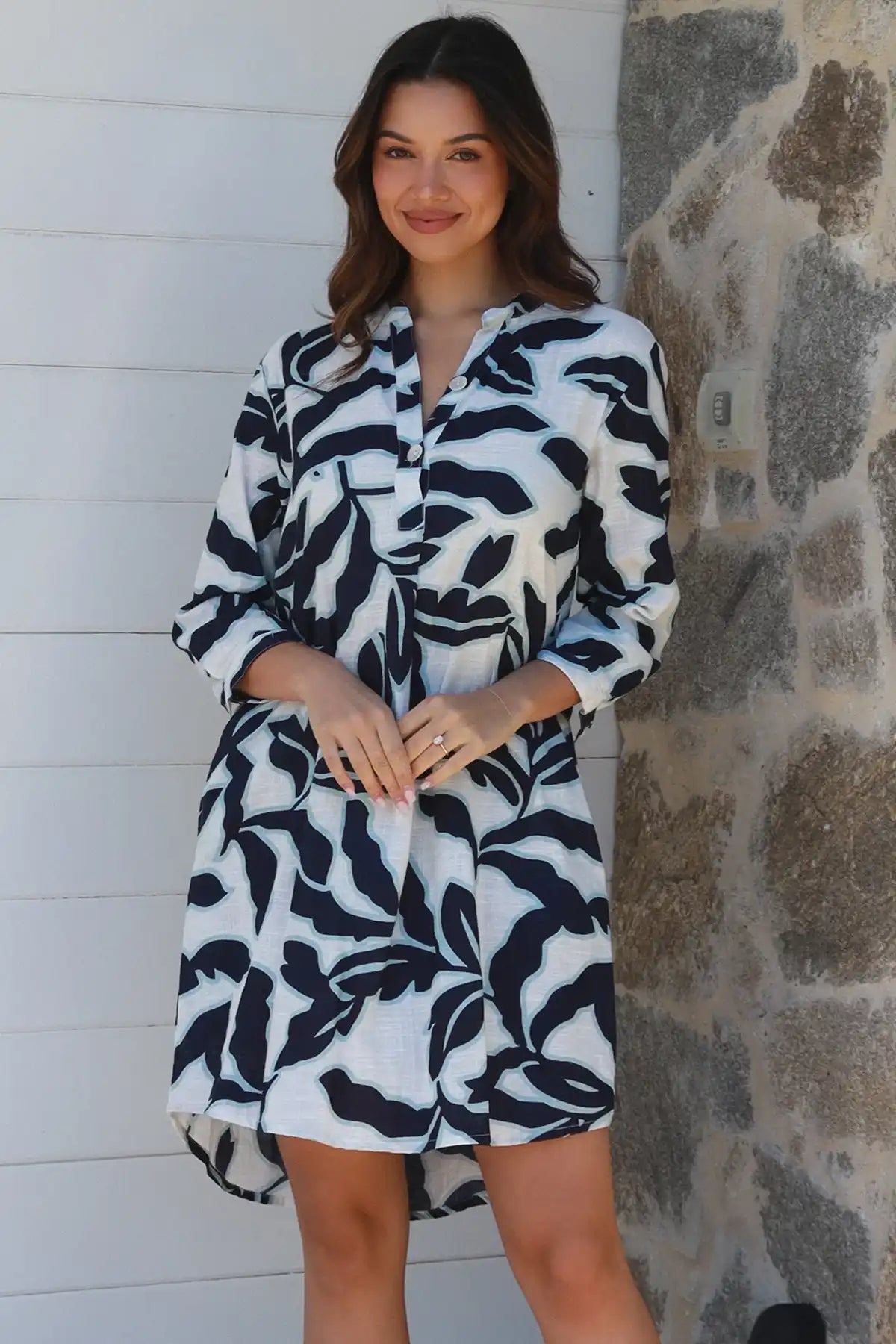 Woman wearing a black and white patterned robe against a stone wall.