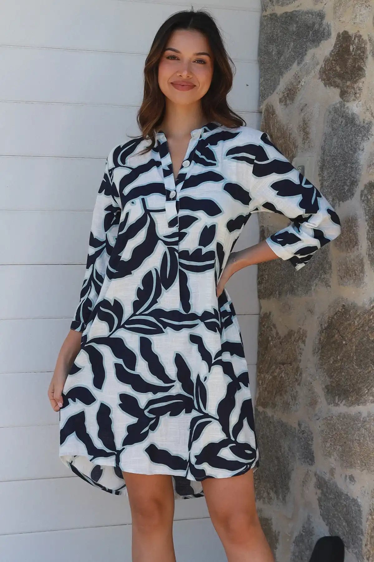 Woman wearing a black and white patterned dress against a stone wall.