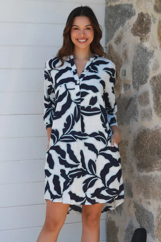 Woman wearing a black and white patterned dress standing against a stone wall.