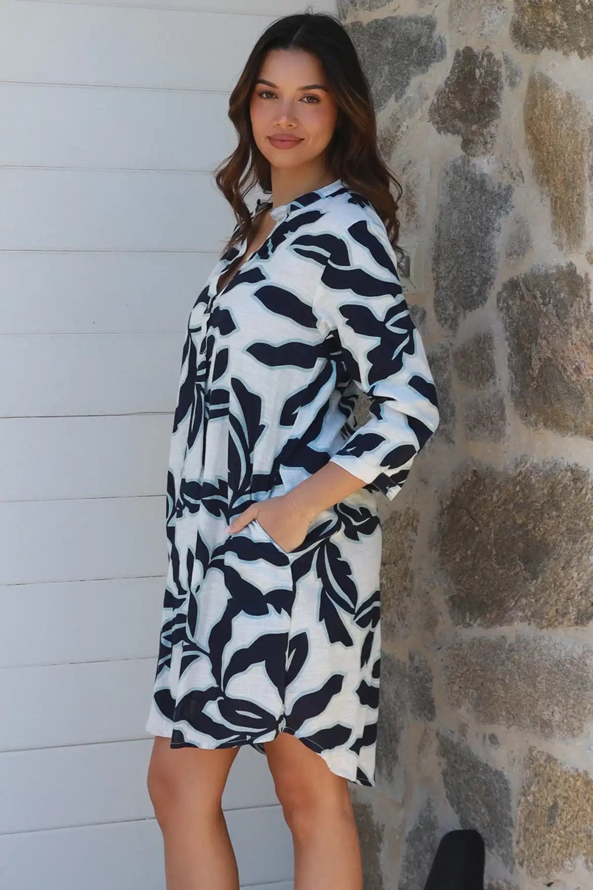 Woman wearing a black and white patterned dress against a stone wall.