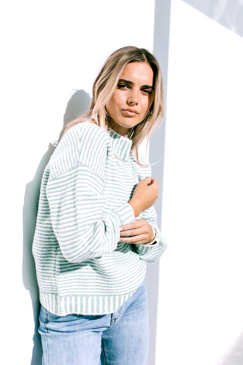 Woman wearing a Billie Stitch Stripe Knit in sage and light blue jeans against a white background