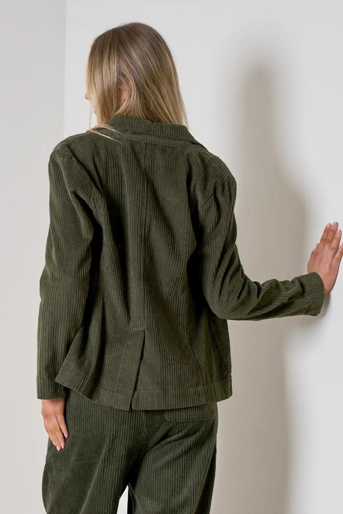 woman wearing Baltic Corduroy Jacket in Forest and pants against a white wall back view