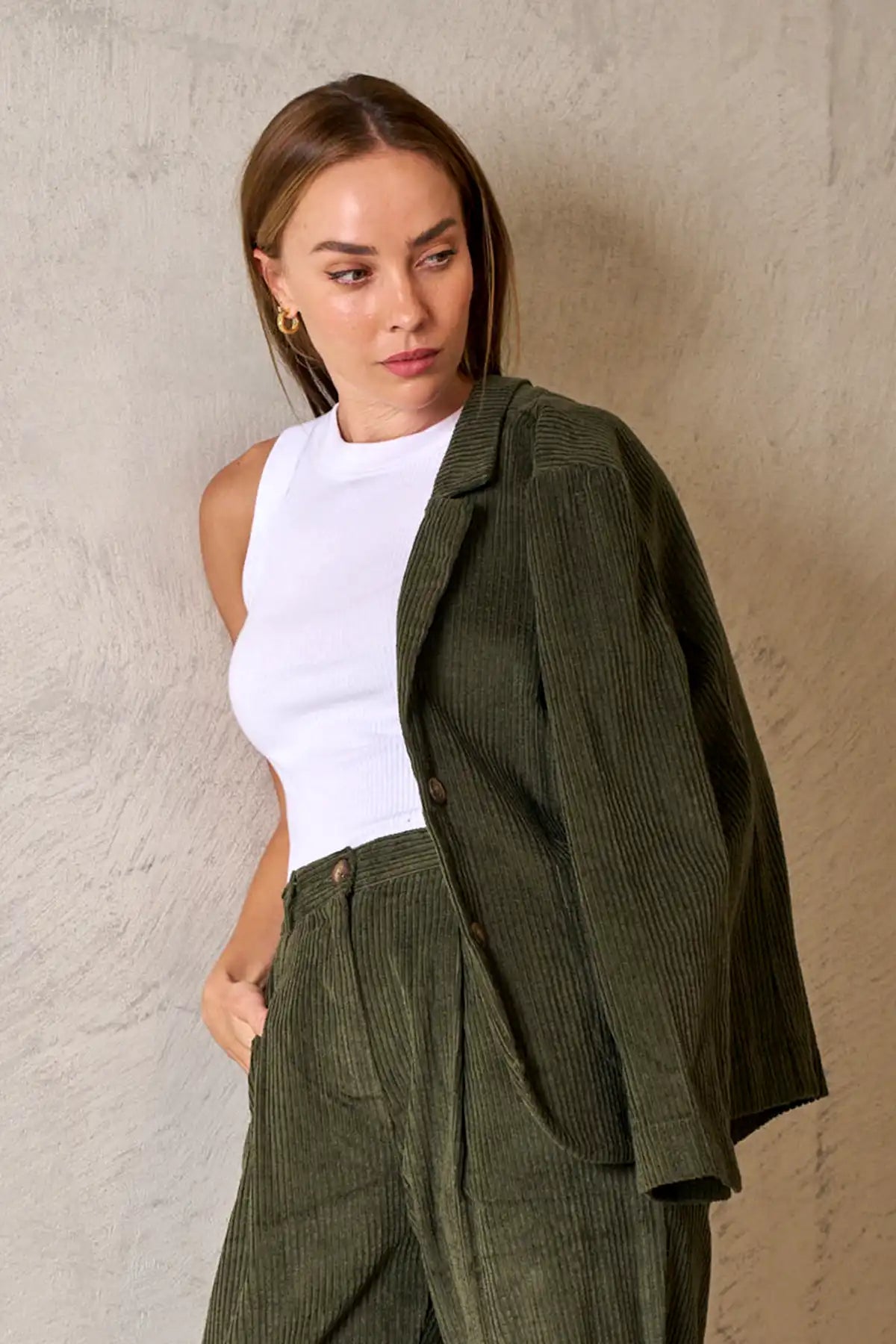 Woman with Baltic Corduroy Jacket in Forest on her shoulder and pants against a beige wall