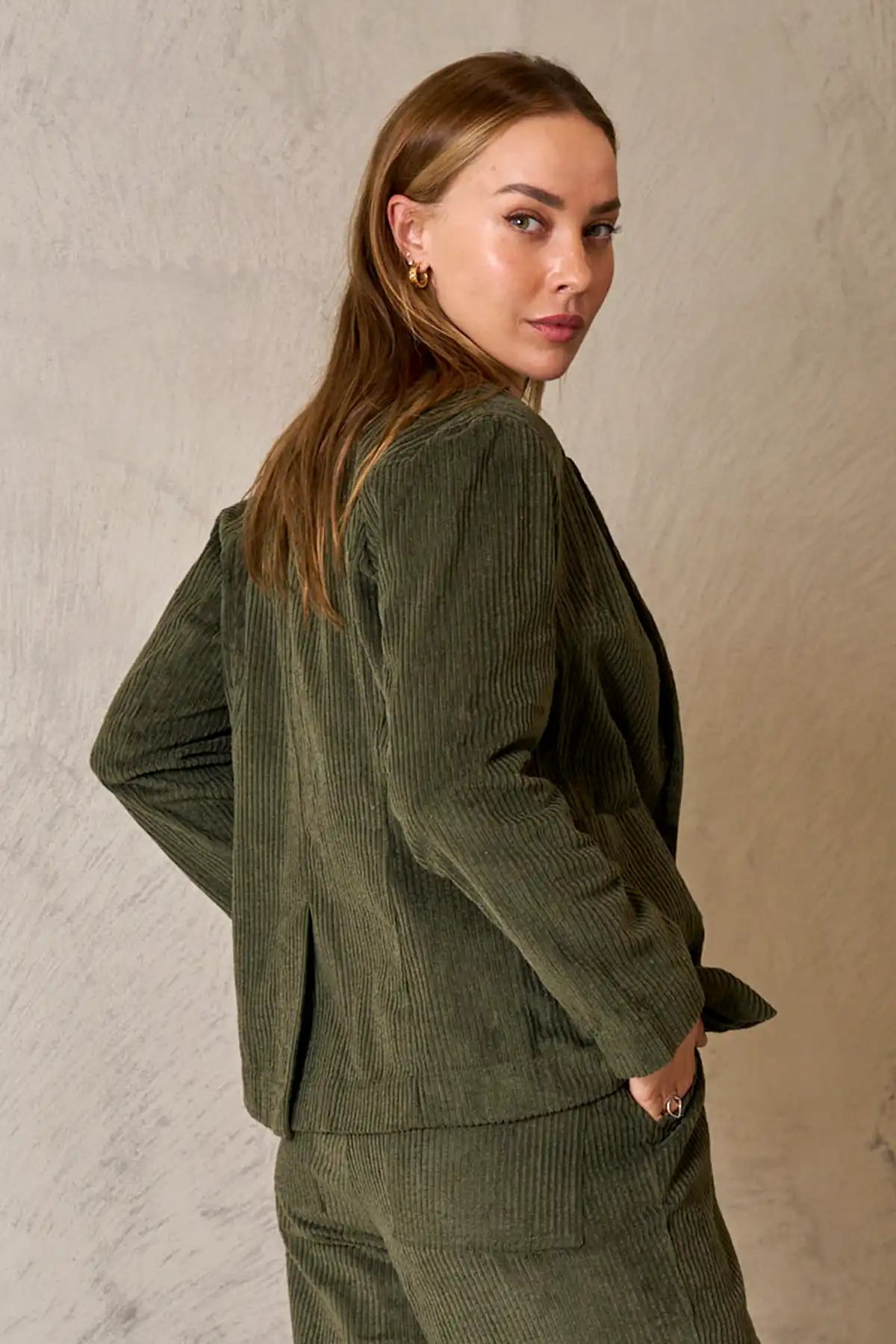 Woman wearing Baltic Corduroy Jacket in Forest outfit against a beige wall