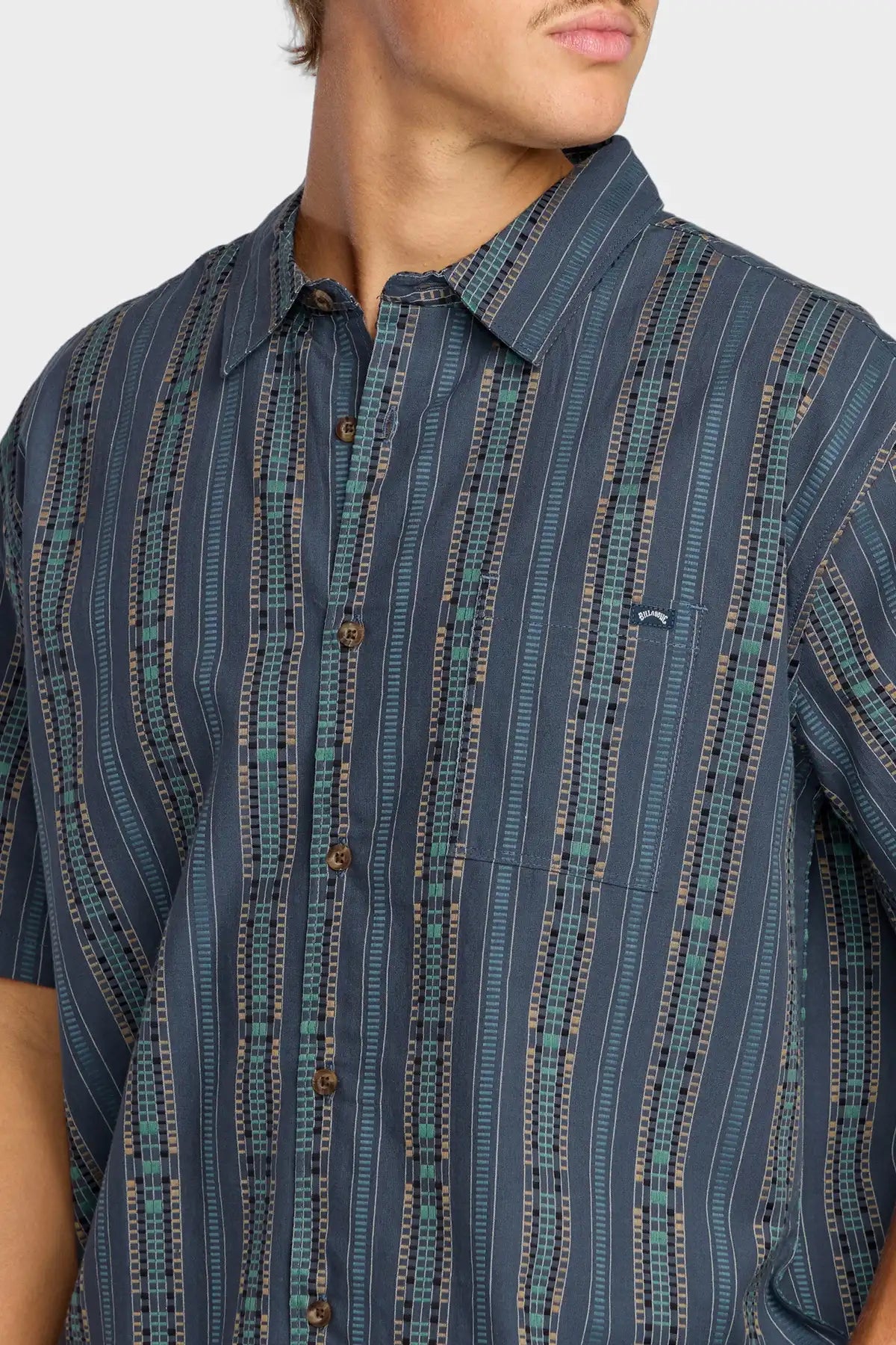 Close-up of a person wearing a dark blue Billabong patterned shirt with a plain background