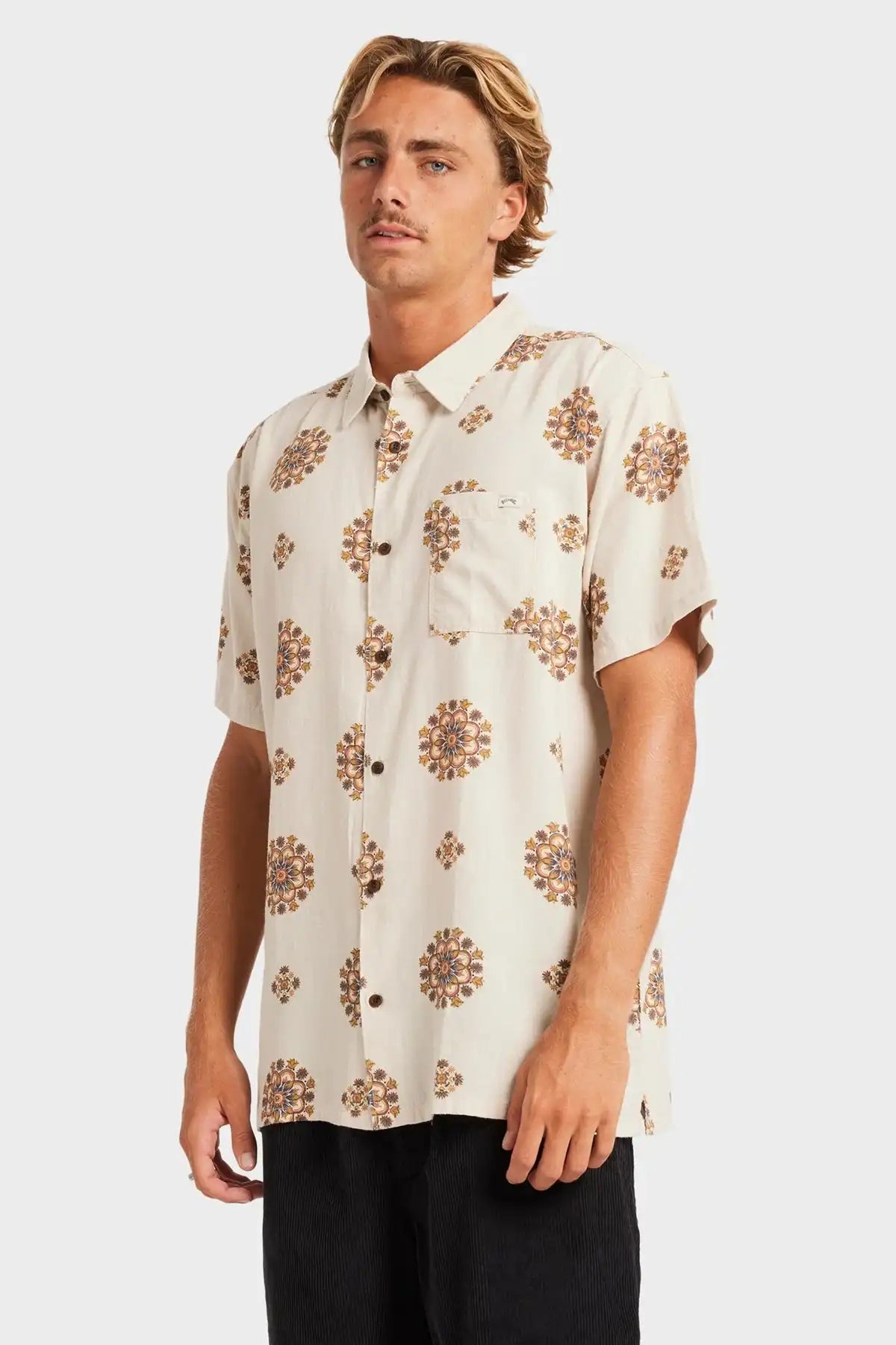Man wearing a beige short-sleeve Billabong shirt with brown floral pattern on a white background