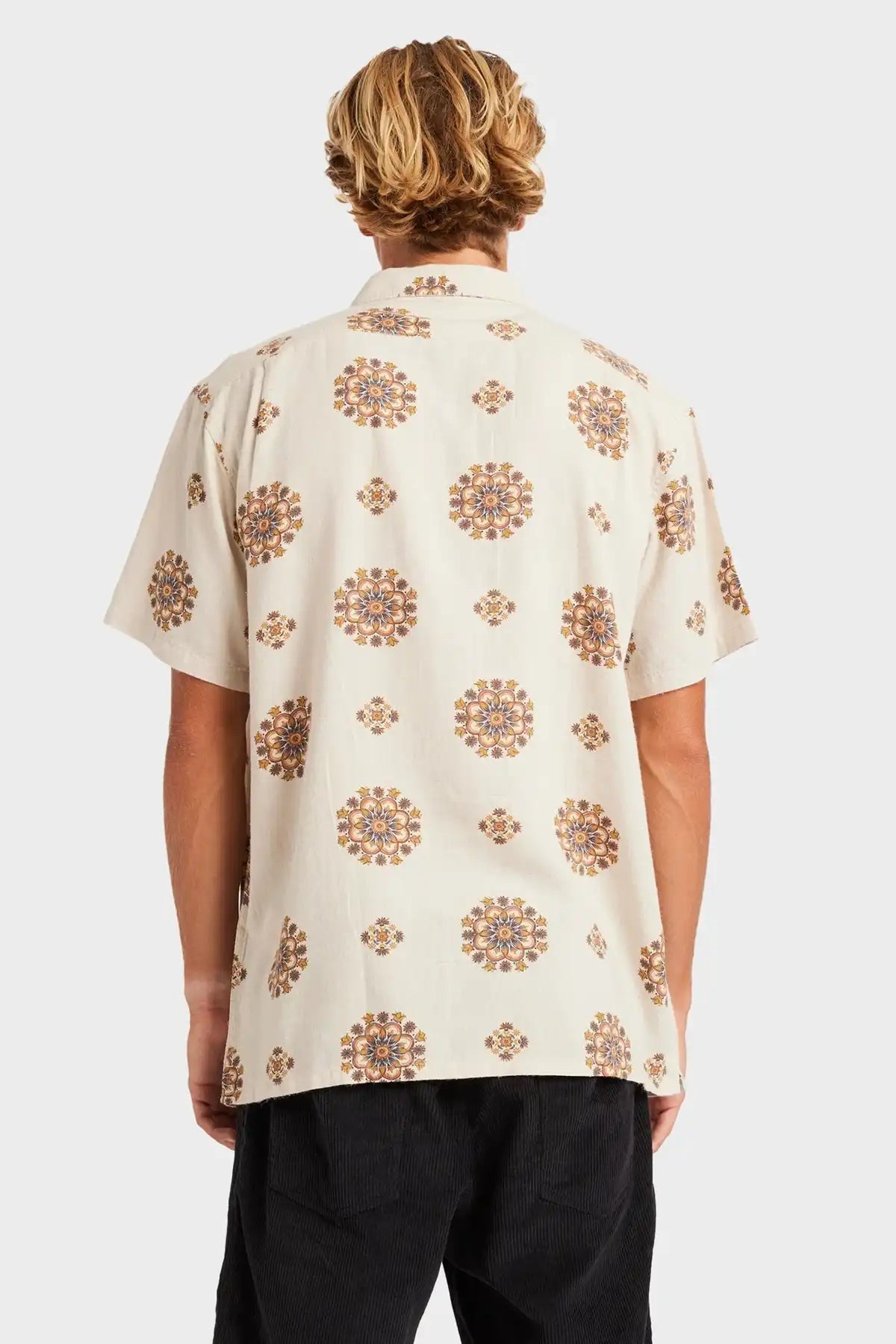 Person wearing a beige shirt with brown floral patterns on a white background