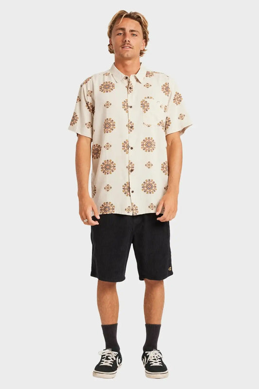 Man wearing a patterned Billabong shirt and black shorts on a white background