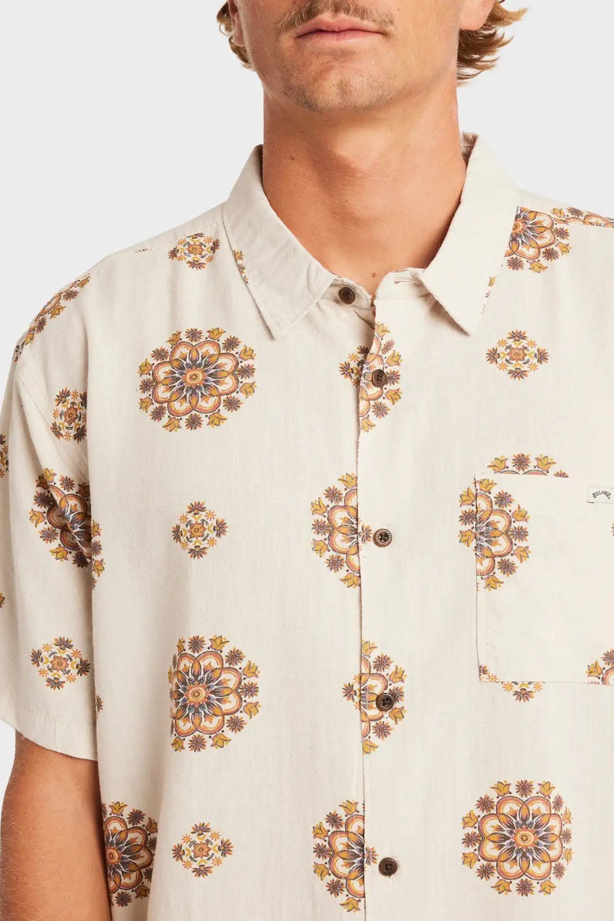 Man wearing a cream-colored Billabong shirt with intricate floral patterns on a plain background