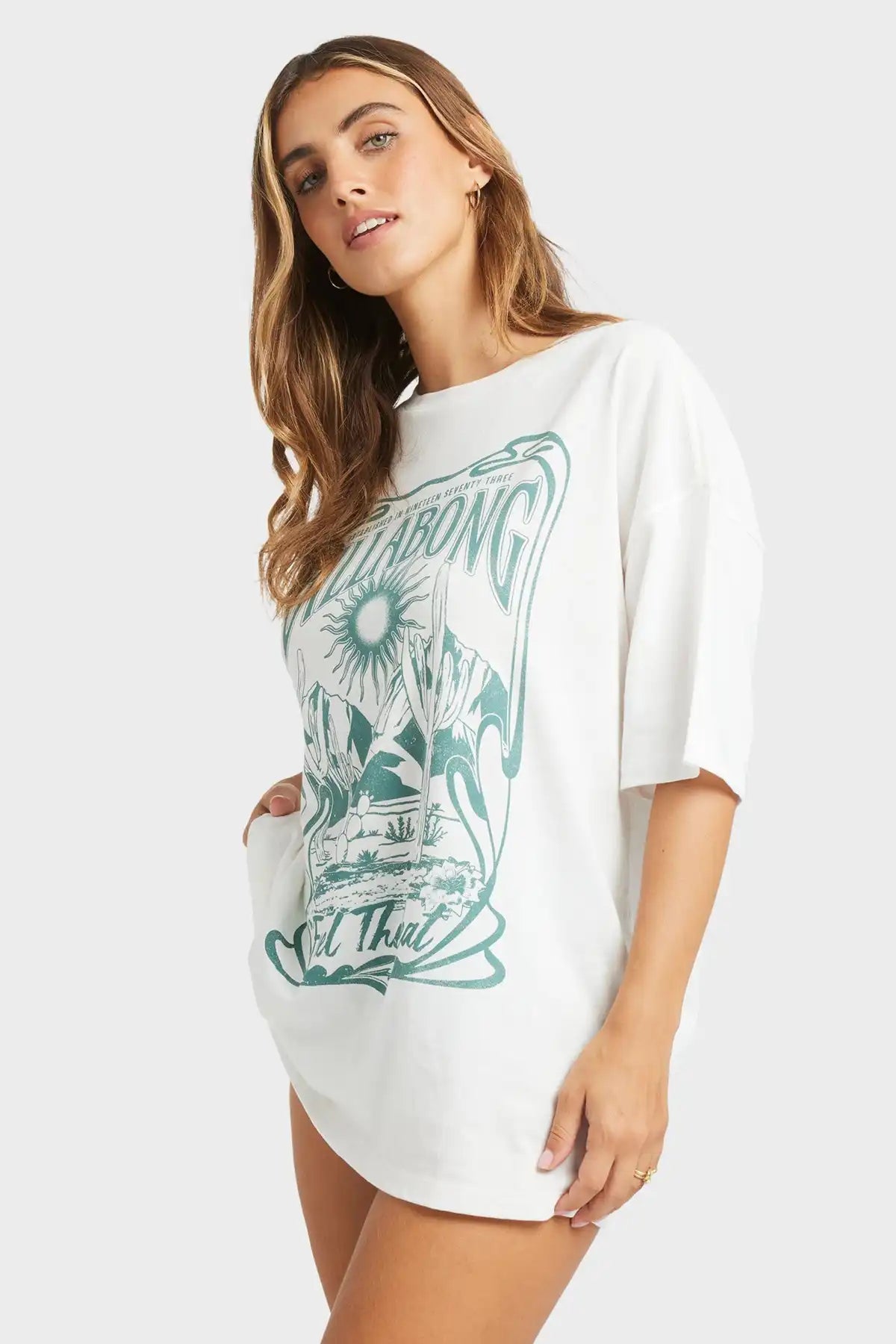 Woman wearing a Salt Crystal Billabong Desert Wandering T-Shirt with green graphic design on a plain background