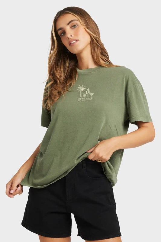 Woman wearing a green Billabong t-shirt with a logo and black shorts on a white background