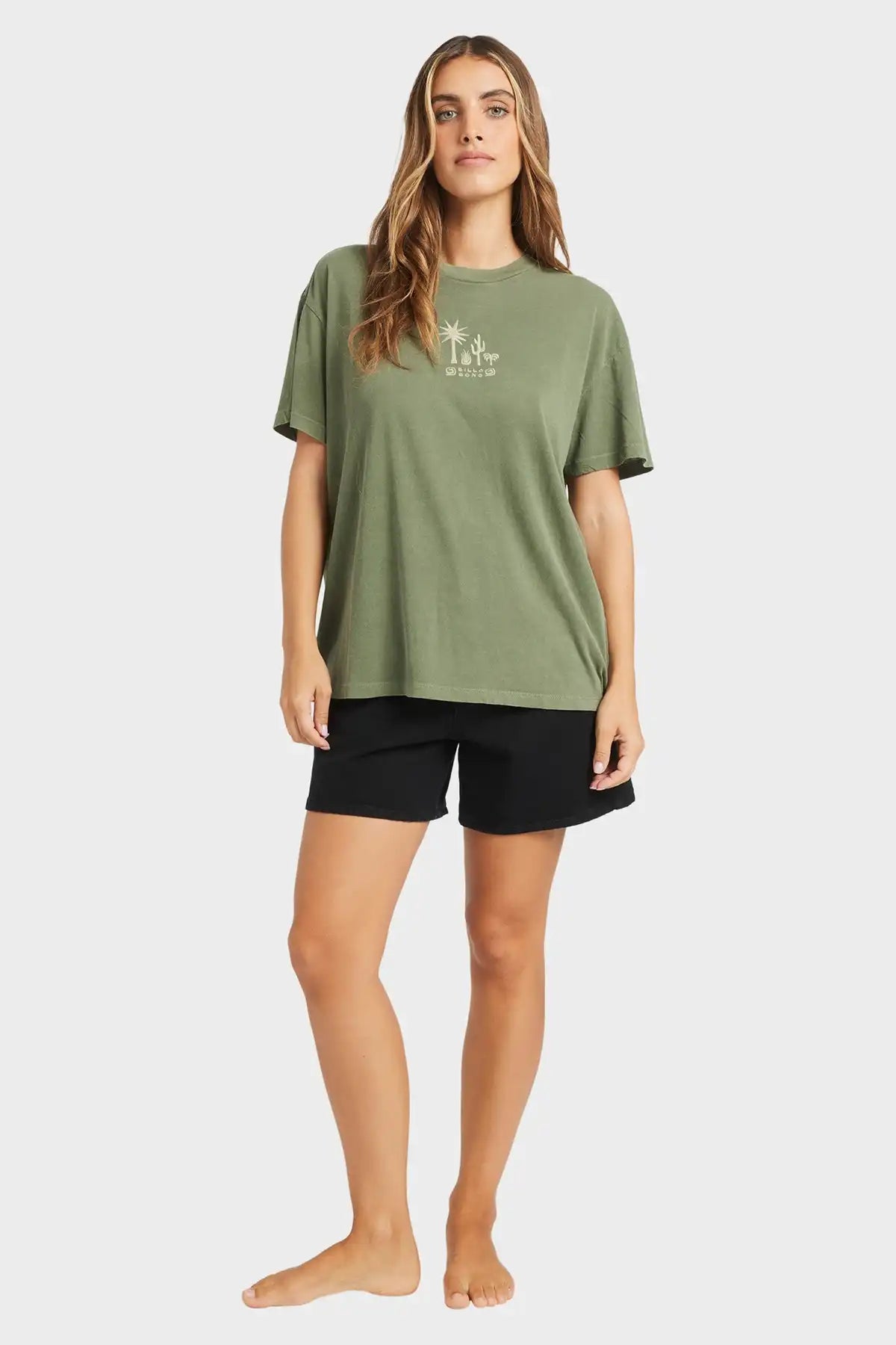 Woman wearing a Billabong green t-shirt and black shorts on a white background