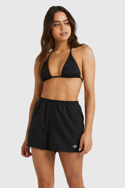 Woman wearing a black bikini with Billabong Womens Sandbar Boardshorts on plain background