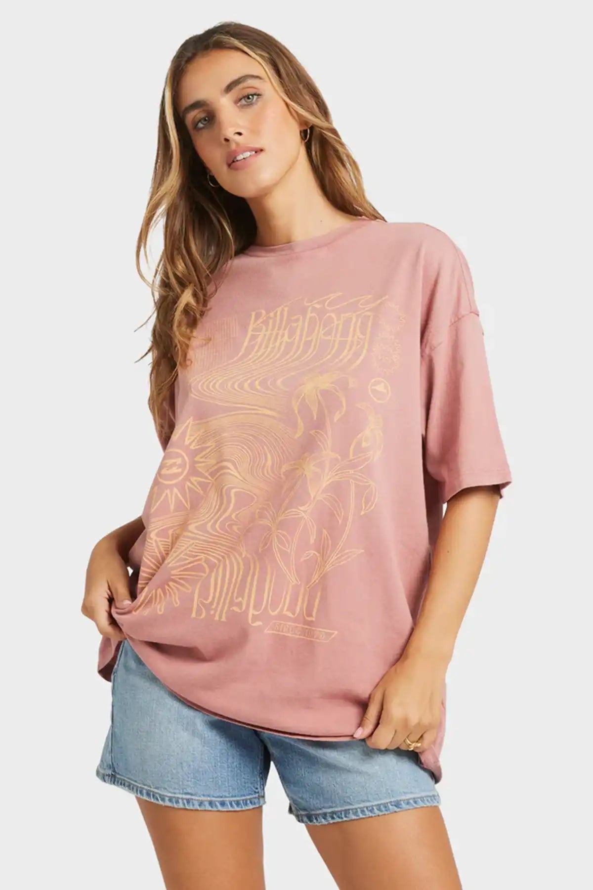 Woman wearing a pink t-shirt with a Billabong graphic design on a white background