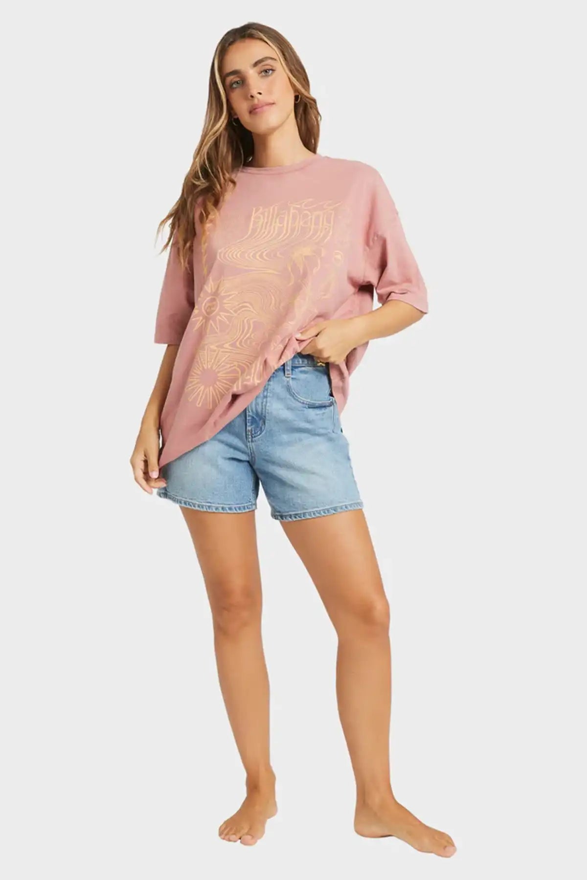 Woman wearing a pink oversized Billabong t-shirt and denim shorts on a white background