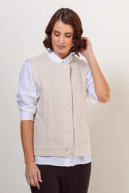Woman wearing a cream cable knit vest over a white shirt on a plain background