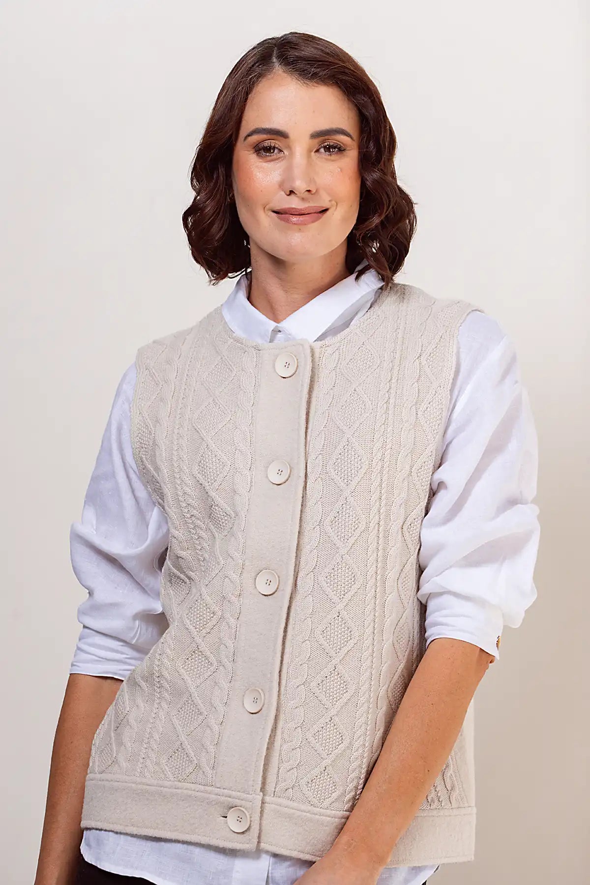 Woman wearing a cream knitted vest over a white shirt on a plain background
