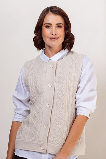 Woman wearing a cream knitted vest over a white shirt on a plain background