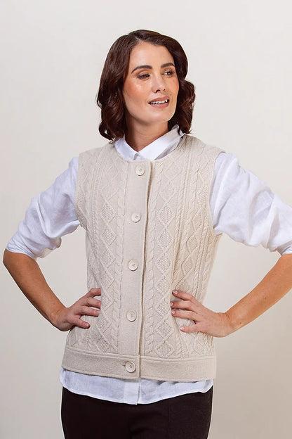 Woman wearing a cream woollen knitted vest over a white shirt on a plain background