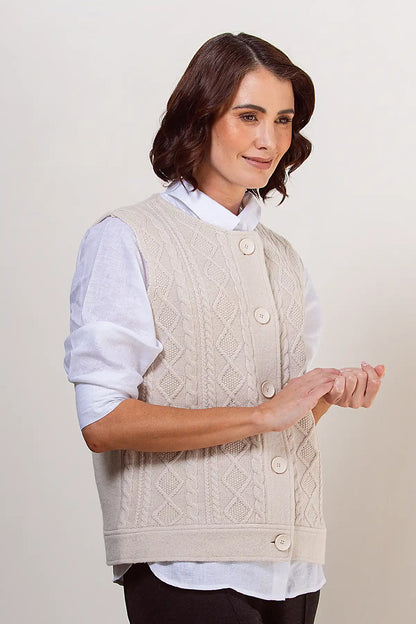 Woman wearing a cream knitted vest over a white shirt on a plain background
