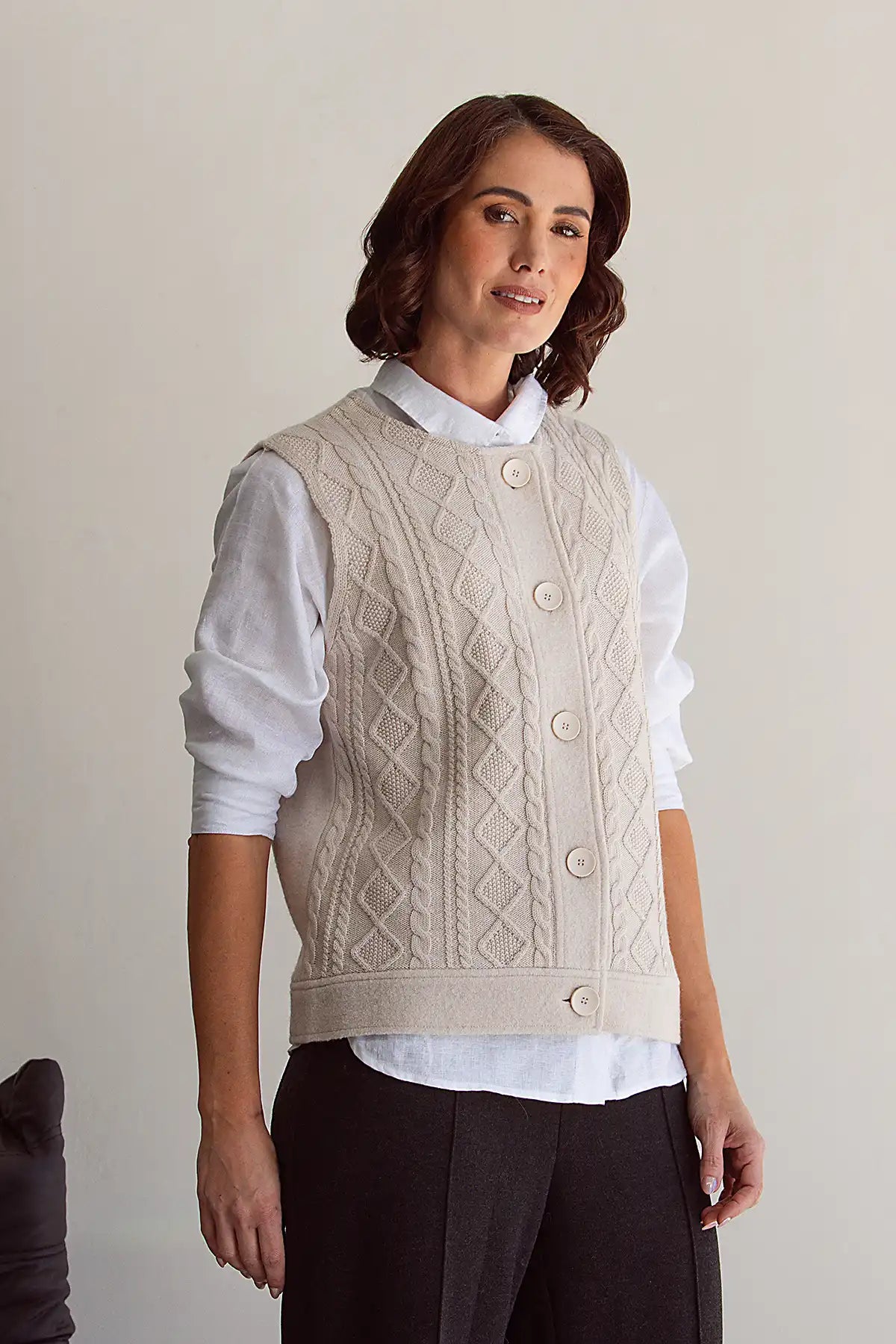 Woman wearing a cream knitted vest over a white shirt with a neutral background
