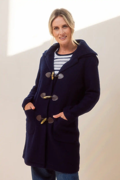 Woman wearing a navy blue boiled wool duffle coat with gold buttons against a plain background