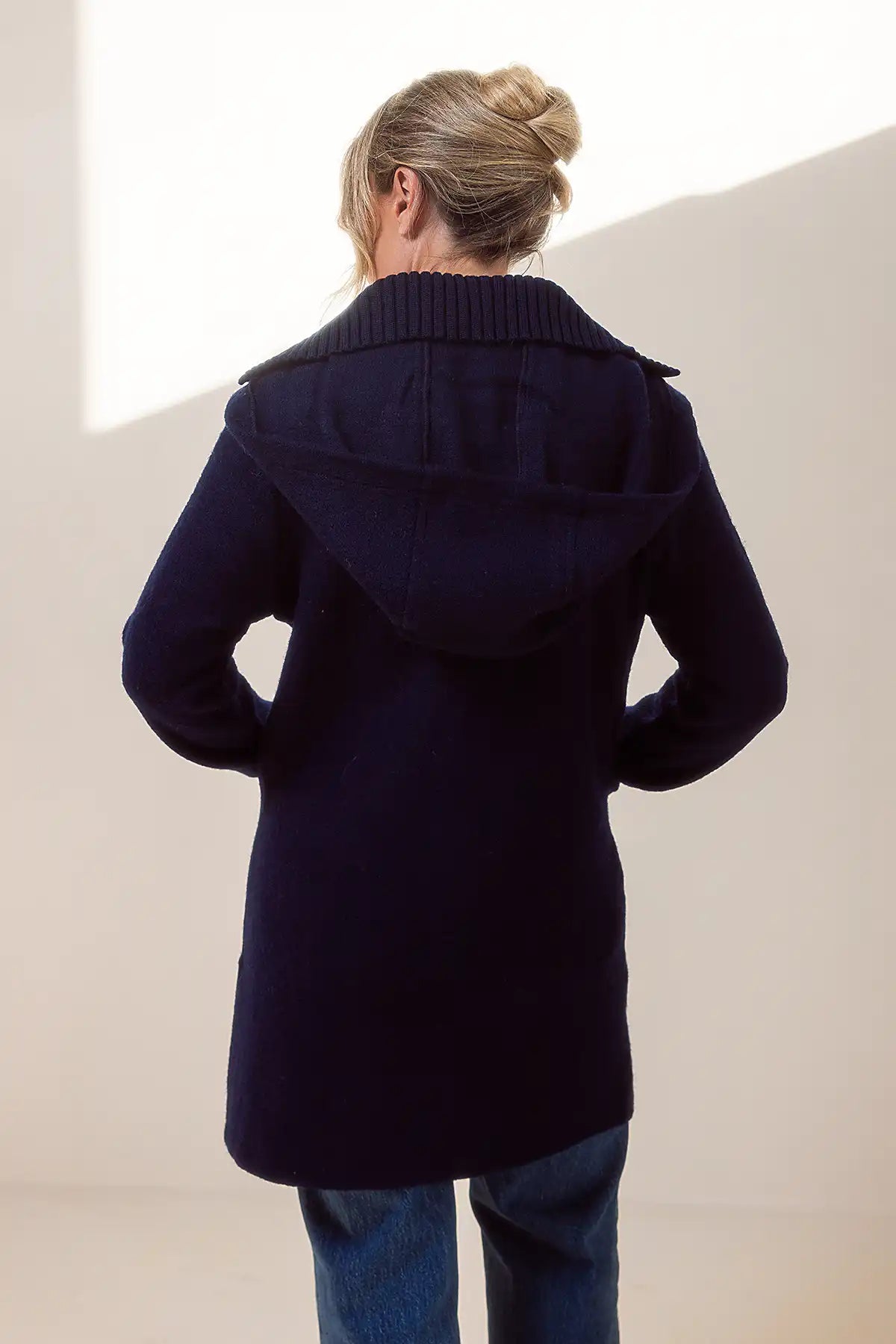 Person wearing a navy blue woolen duffle coat with a plain background