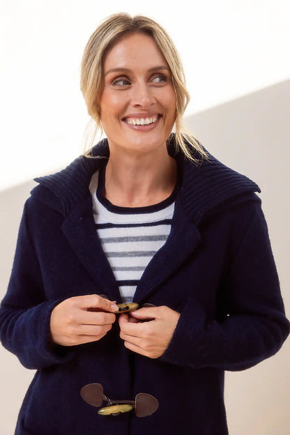 Woman wearing a navy blue duffle coat over a striped shirt on a plain background