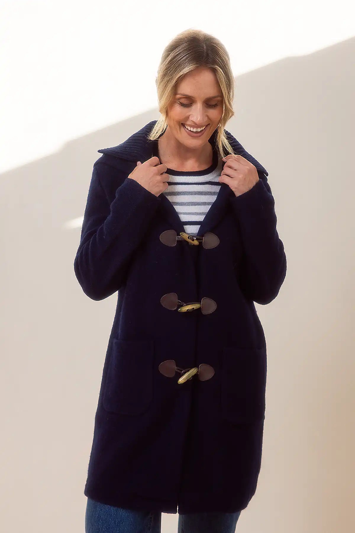 Woman wearing a navy blue duffle coat with gold buttons on a beige background