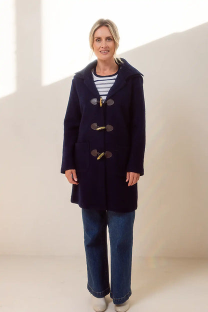 Woman wearing a navy blue coat with large buttons on a plain background