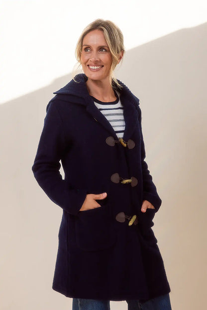 Woman wearing a navy blue boiled wool coat with wooden toggel buttons against a beige background