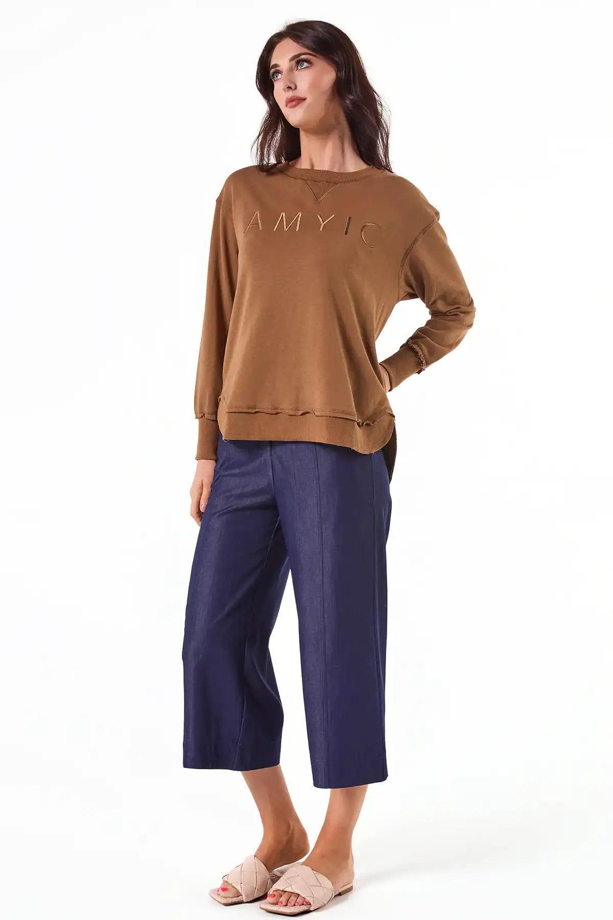 Woman wearing a Chille Everyday Wander Pullover in Mocha with embroidery on front and blue pants on a white background