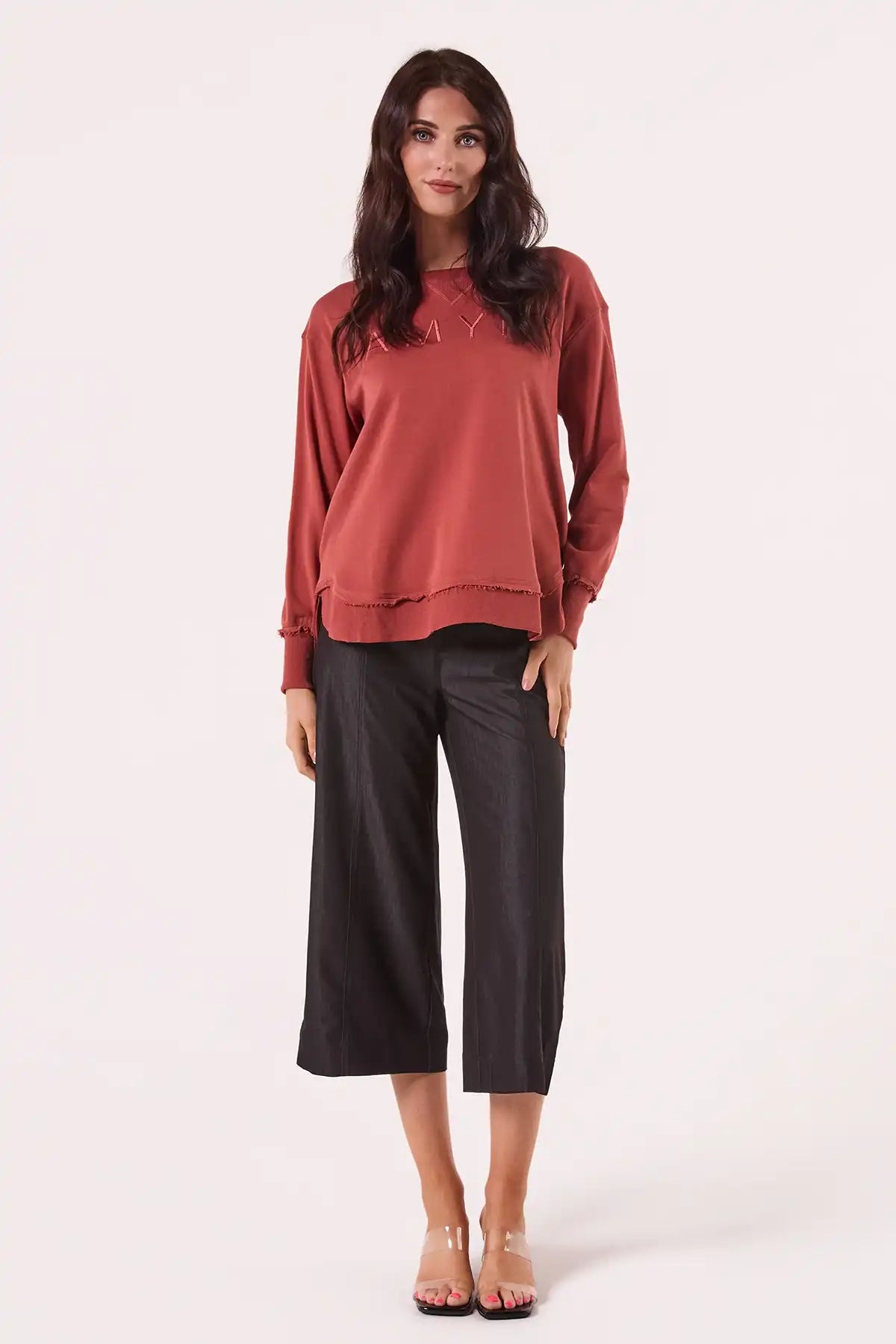 Woman wearing a Chille Everyday Wander Pullover in Rust with embroidery logo  black pants on a white background full model view