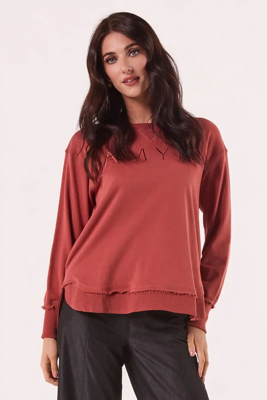 Woman wearing a Chille Everyday Wander Pullover in Rust with embroidery logo on a light pink background