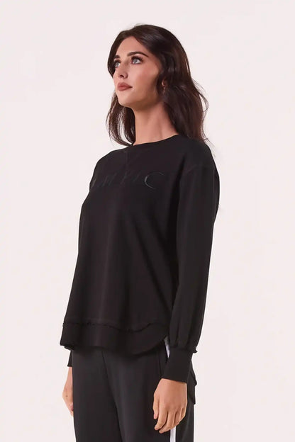 Woman wearing a Chille Everyday Wander Pullover in Midnight Black with a subtle design on a light pink background side view