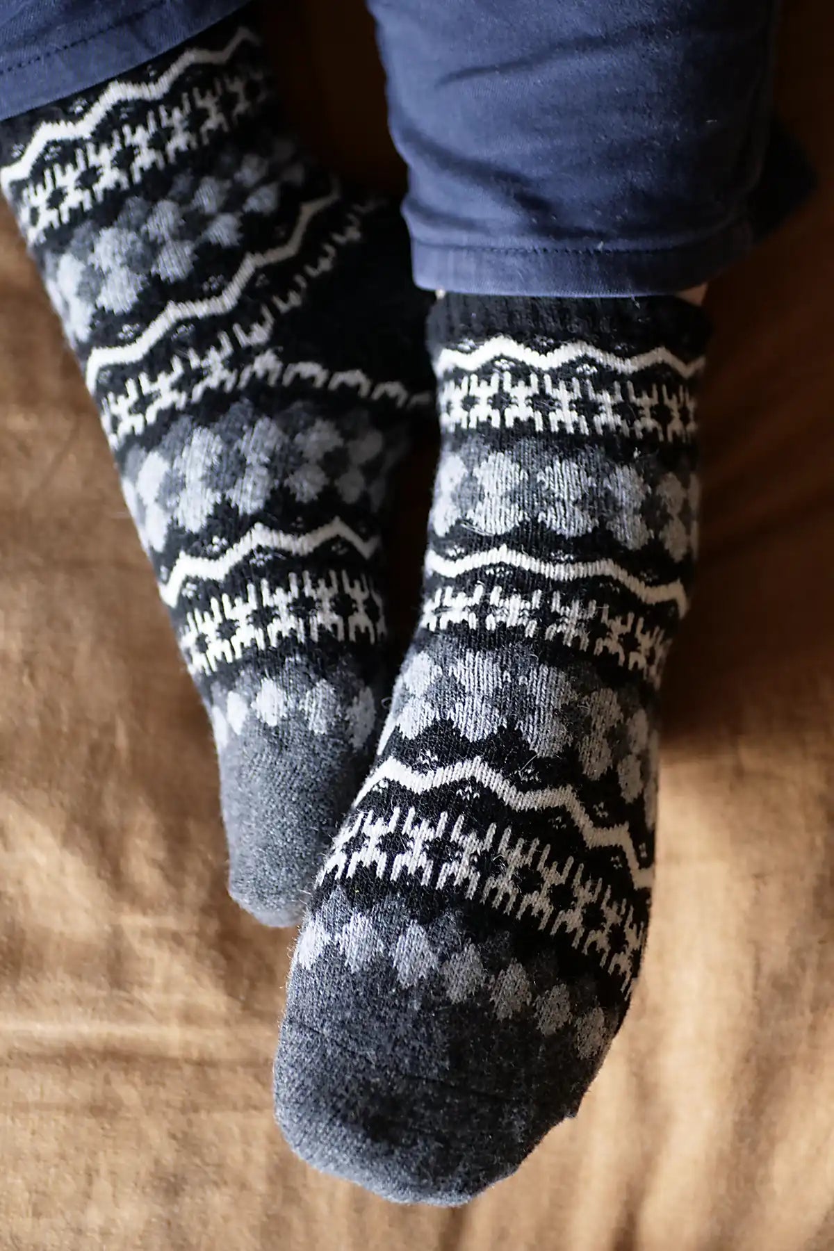 Pair of dark gray socks with white patterns worn by a person on a wooden floor.