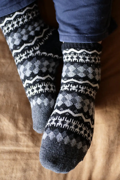 Pair of dark gray socks with white patterns worn by a person on a wooden floor.