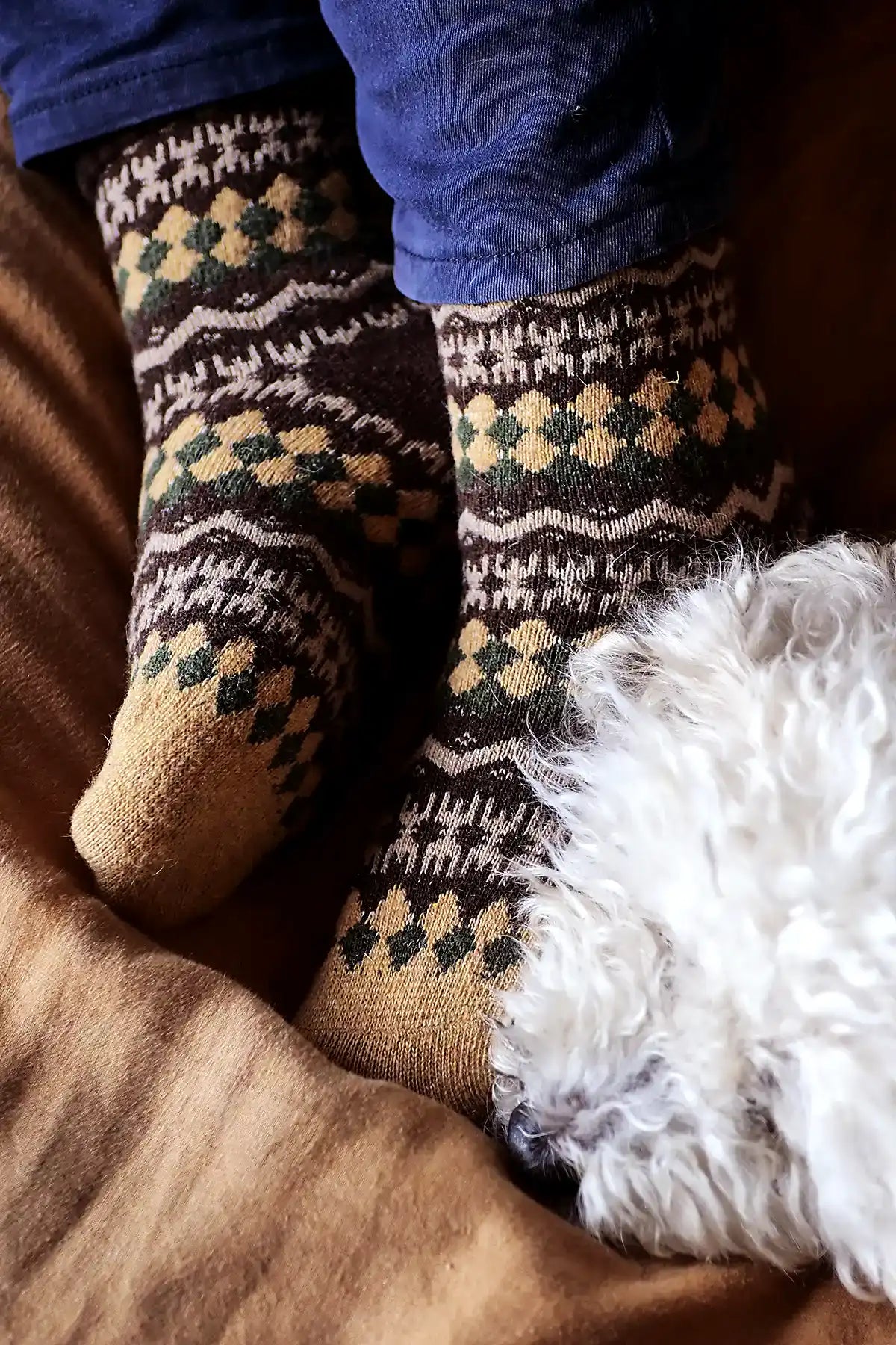 Person wearing patterned socks sitting on a brown surface with a white fluffy object.