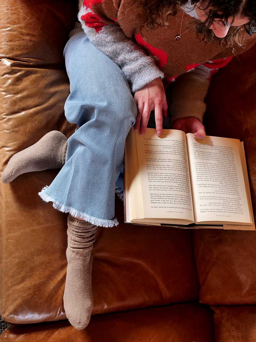 model sitting on coach with good book wearing Chille Wool Blend Socks in Coffee