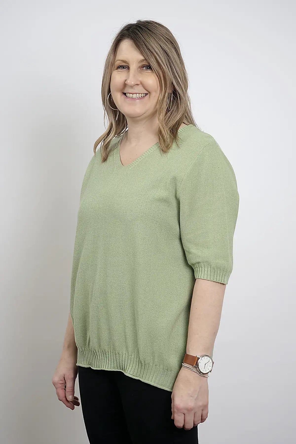 Woman wearing a Coastal Ease Cotton Knit Tee in Sage Green against a plain background