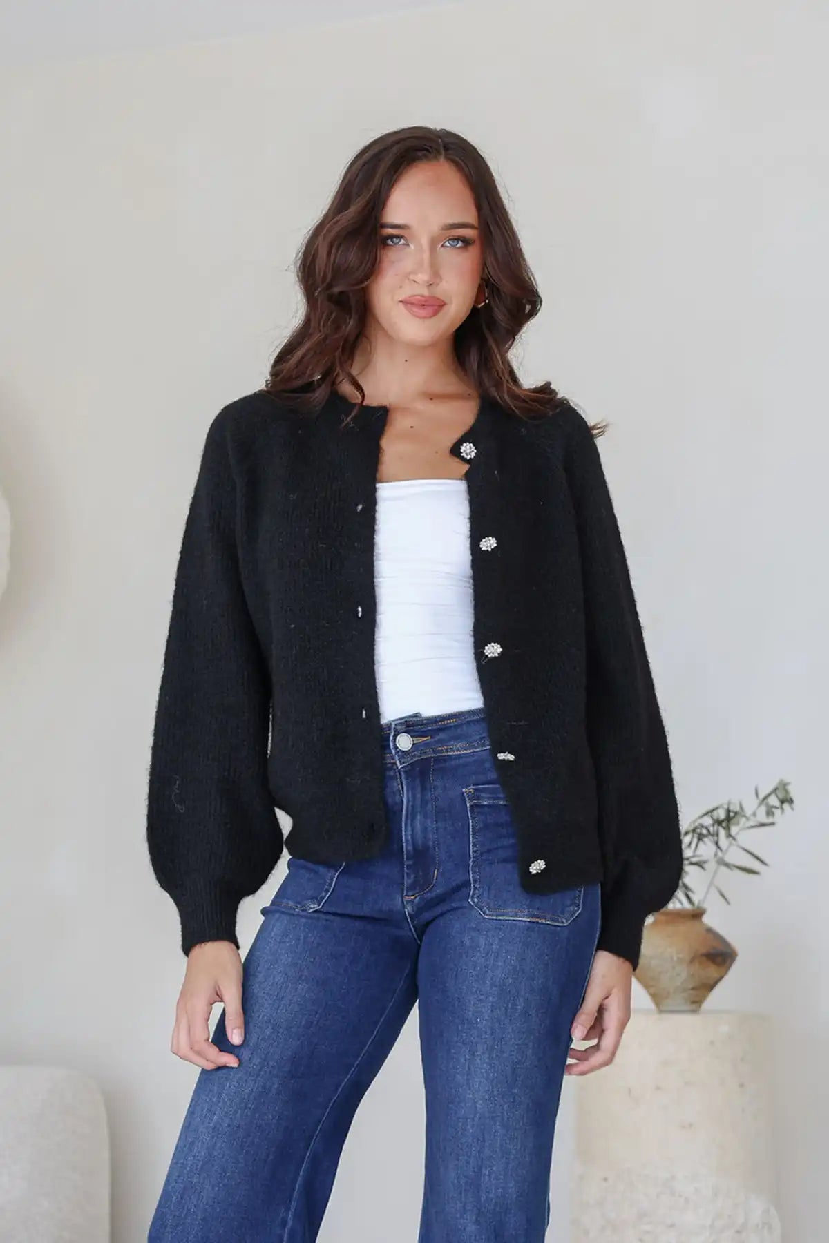 Woman wearing a Diamonte Button Rib Cardi in black, white top, and blue jeans indoors.
