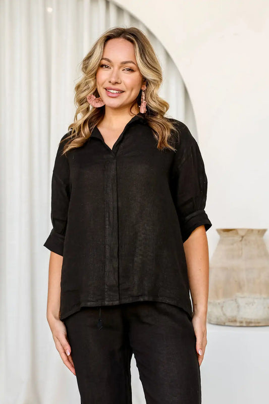 Woman wearing a Drift Italian Linen Top – Black and pants standing against a white curtain.