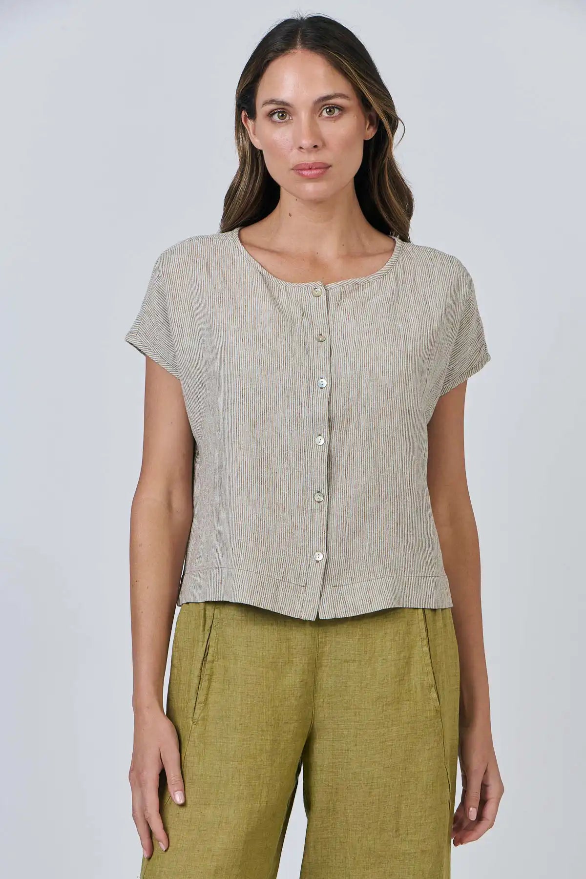 Woman wearing a Elysian Linen Top – Blister Stripe and green pants against a white background
