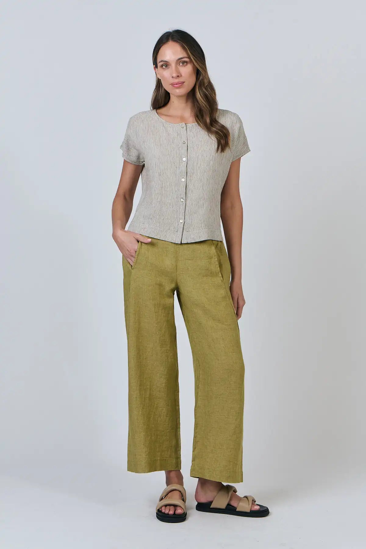 Woman wearing a Elysian Linen Top – Blister Stripe and green pants on a white background full model view