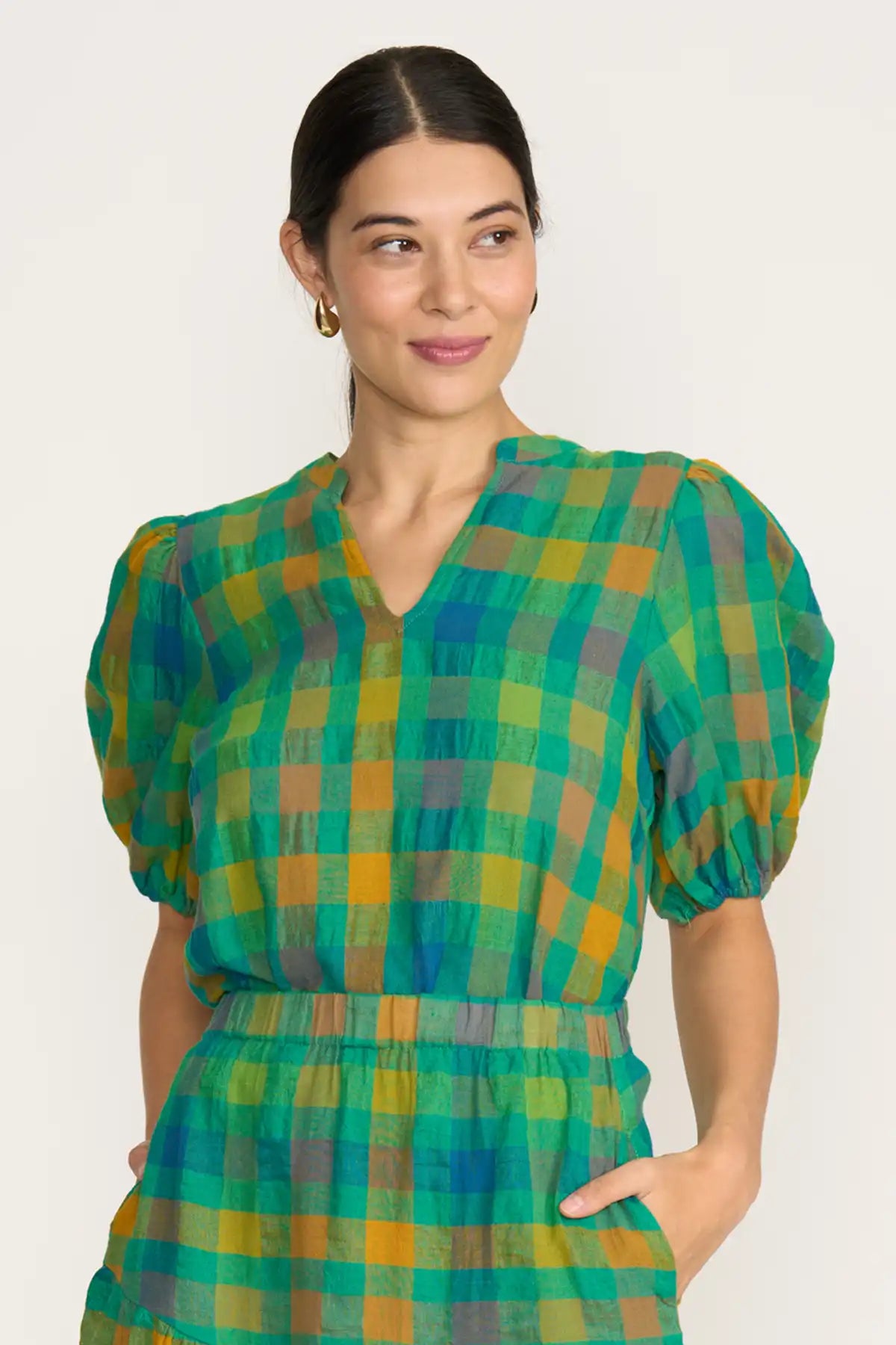 Woman wearing a Foil Checkmate Top – Green Check against a white background