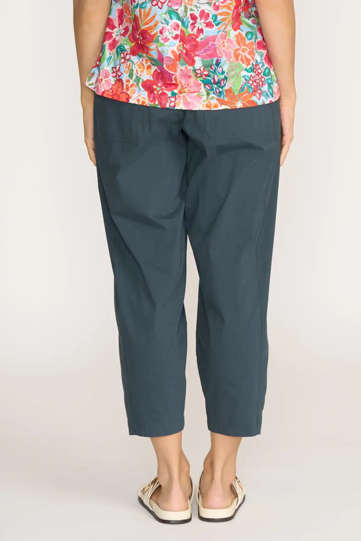 Person wearing Foil Gemini Pants in Basalt  (back view) and a colorful floral top on a plain background