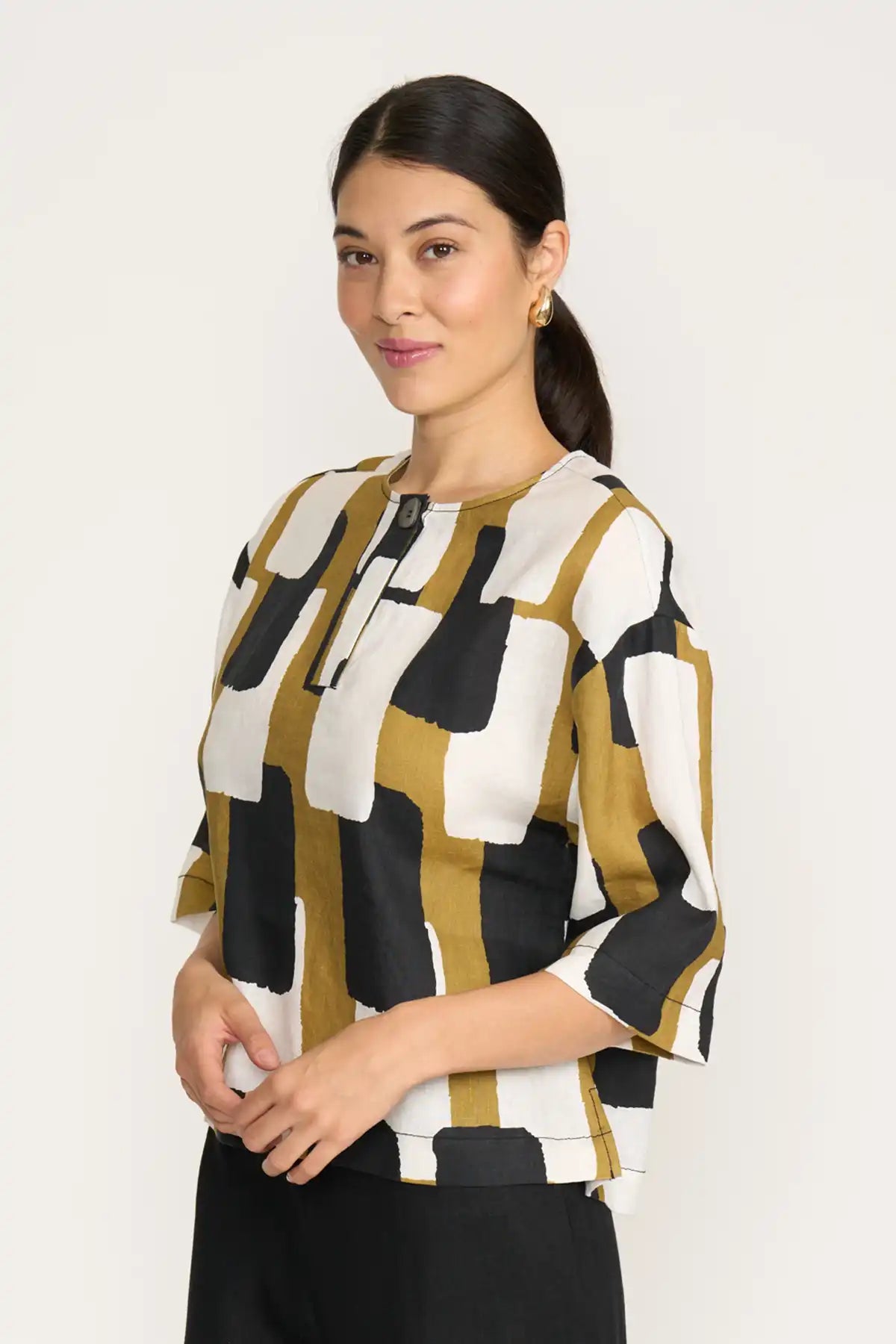 Woman wearing a Foil Looking Sharp Top in Art Box Print with black, white, and mustard yellow colors on a plain background side 3/4 view